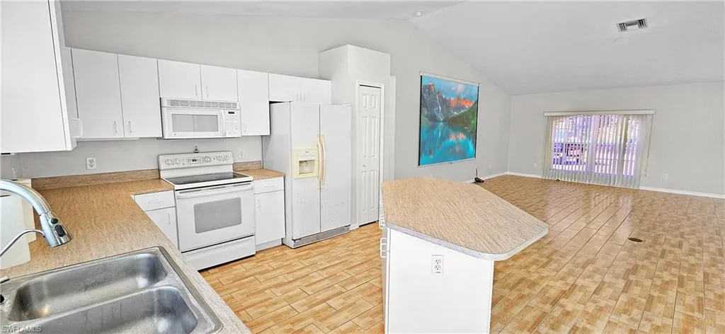 Kitchen featuring white appliances, open floor plan, light countertops, white cabinetry, and wood finish floors