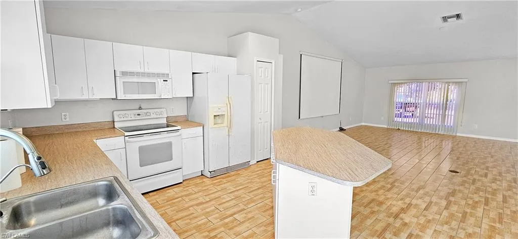 Kitchen featuring white appliances, open floor plan, light countertops, white cabinetry, and light wood finished floors