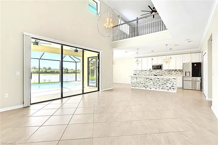 Unfurnished living room with ceiling fan, crown molding, light tile patterned floors, a sunroom, and a high ceiling