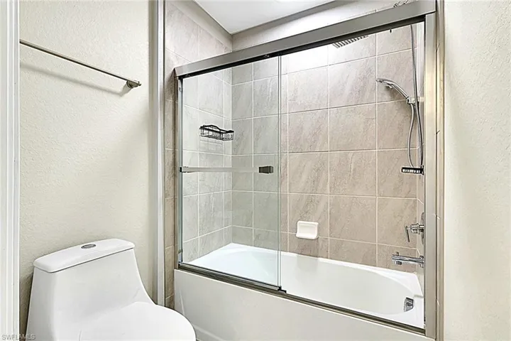 Bathroom with a textured wall and shower / bath combination with glass door