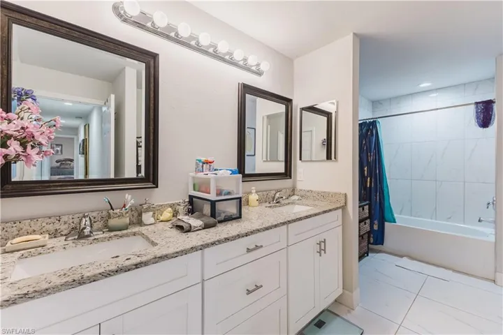 Bathroom with shower / bath combination with curtain, double vanity, and light marble finish flooring