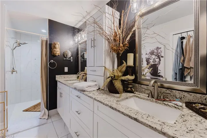 Full bath featuring double vanity, a stall shower, and light marble finish flooring