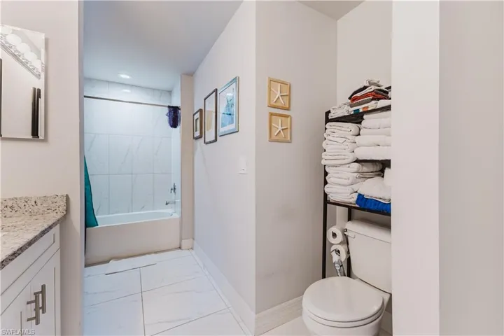 Bathroom featuring shower / tub combo with curtain, vanity, light marble finish floors, and recessed lighting