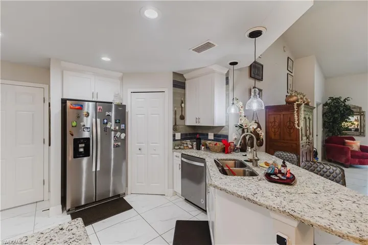Kitchen with stainless steel appliances, light stone countertops, hanging light fixtures, a breakfast bar, and a peninsula