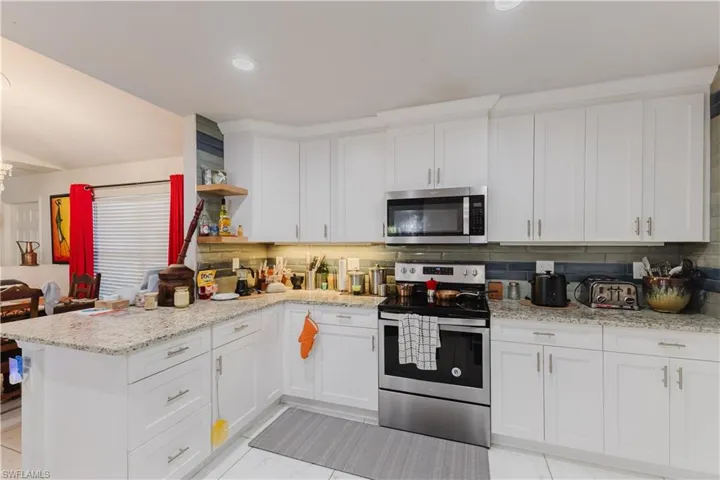 Kitchen featuring open shelves, appliances with stainless steel finishes, white cabinetry, light stone counters, and recessed lighting