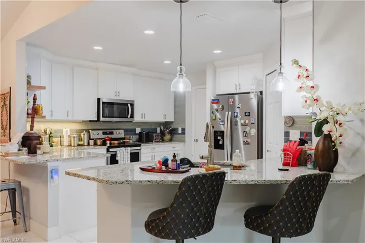 Kitchen featuring a peninsula, a kitchen breakfast bar, stainless steel appliances, white cabinets, and decorative backsplash