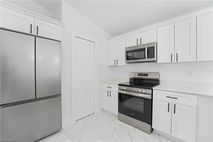 White cabinetry with black hardware, stainless steel appliances, light-toned countertops, and marble-look tile flooring