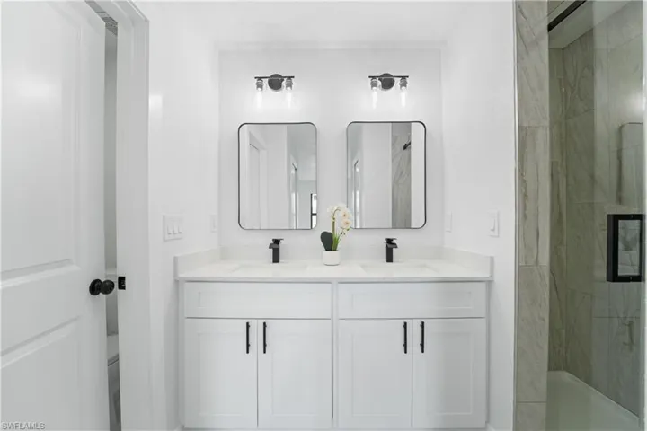 Double vanity with white cabinetry, matte black hardware, and individual mirrors