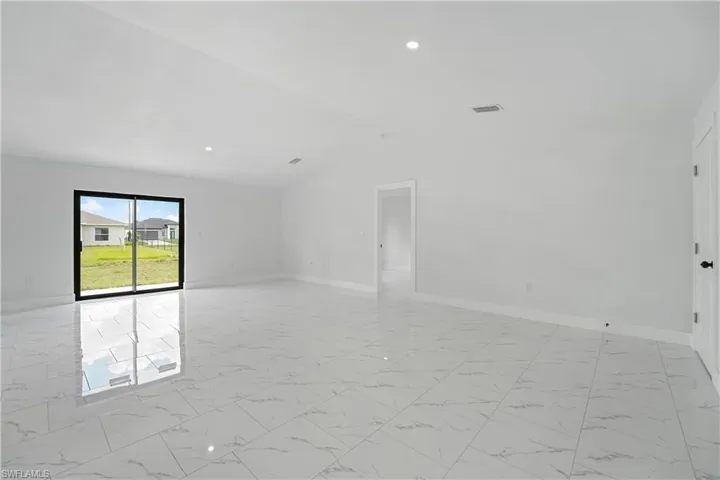 Spacious room featuring vaulted ceilings, recessed lighting, large format tile flooring, and sliding glass door access to the exterior