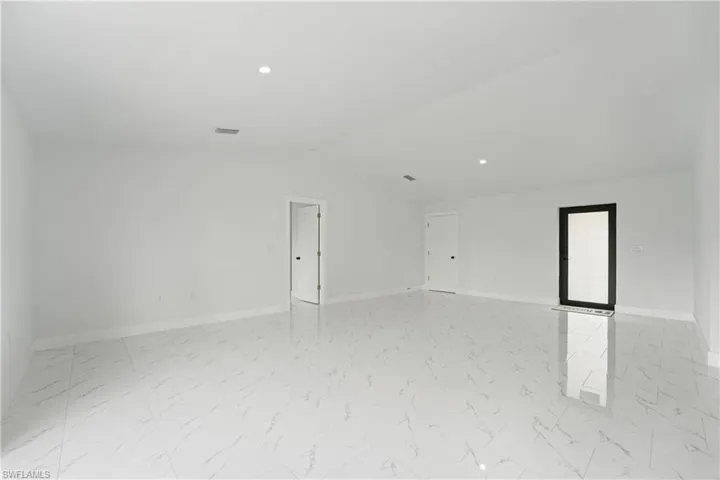 Spacious room with white walls, recessed ceiling lighting, and white tile flooring