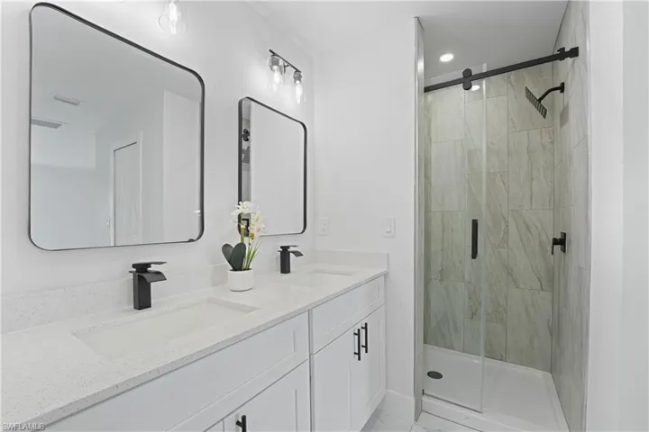 Dual vanity with integrated sinks and black matte faucets, under-counter storage, framed mirrors, and a shower with a sliding glass door and tile surround