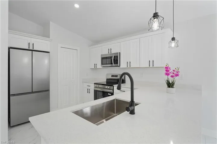 White cabinetry, stainless steel appliances, integrated stainless steel sink, matte black faucet, and pendant lighting
