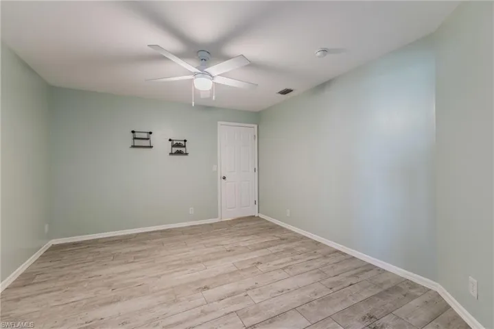 Room featuring wood-finish flooring, a white ceiling fan with integrated lighting, and a six-panel interior door