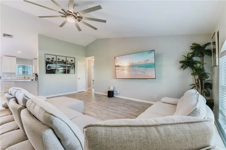 Living area featuring vaulted ceilings, wood-finish flooring, and a multi-blade ceiling fan