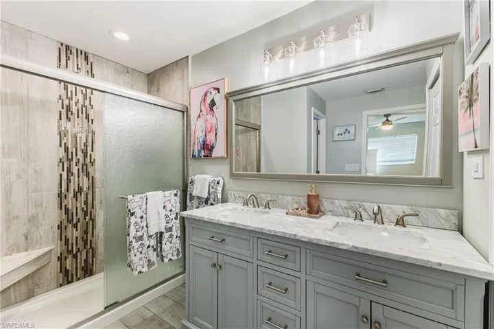 Double vanity with a stone countertop and dual under-mount sinks, framed vanity mirror, overhead vanity lighting, and a walk-in shower with decorative vertical tile inlay