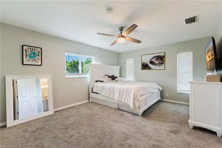 Bedroom featuring neutral wall paint, carpeted flooring, a ceiling fan with integrated light, and three windows equipped with horizontal blinds