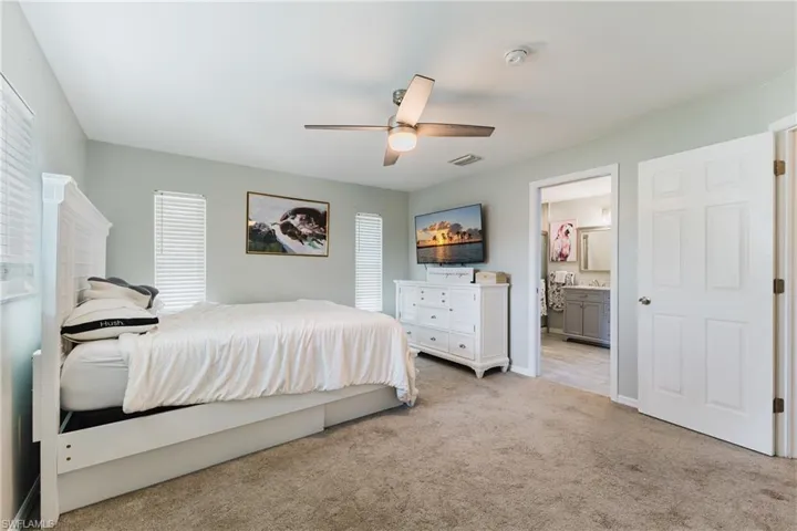 Bedroom featuring neutral wall paint, carpeted flooring, a ceiling fan with integrated lighting, and multiple windows with horizontal blinds