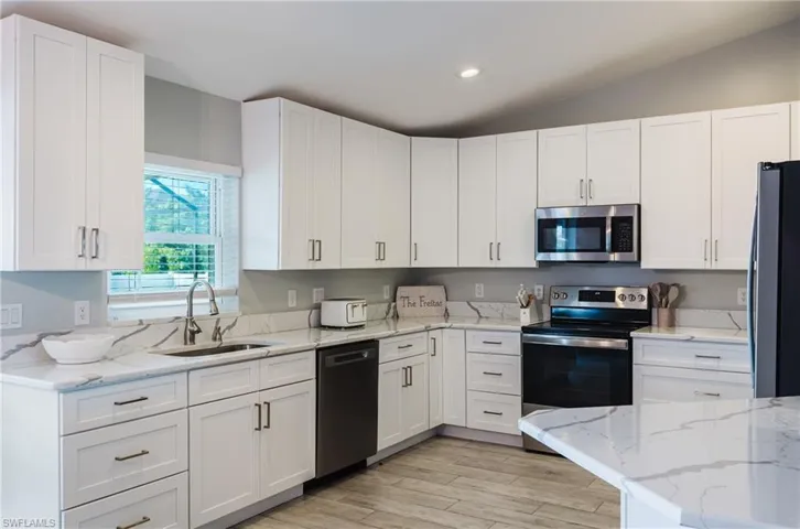 Kitchen featuring white shaker-style cabinetry, white countertops with grey veining, stainless steel appliances, and wood-finish tile flooring