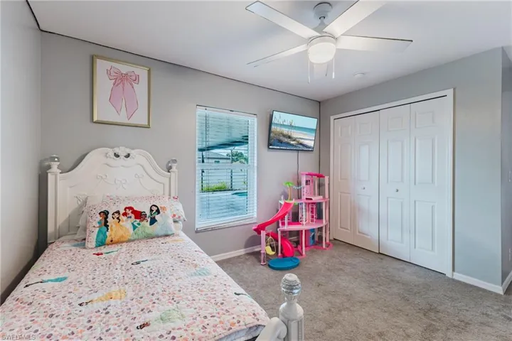 Bedroom featuring neutral wall paint, carpeted flooring, a ceiling fan with integrated lighting, and white multi-panel bi-fold closet doors