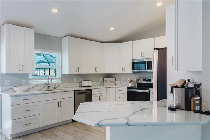 Kitchen featuring white shaker-style cabinetry, white countertops with grey veining, stainless steel appliances, recessed lighting, and wood-finish flooring