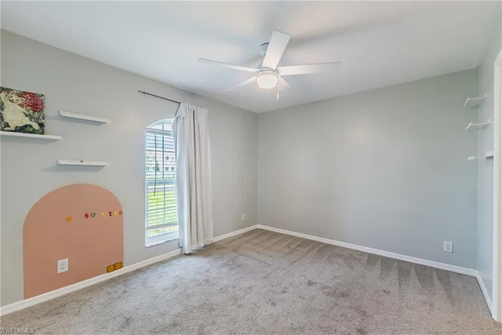 Room featuring neutral wall tones, wall-to-wall carpeting, an arched window, built-in shelving, and a ceiling-mounted light fixture with fan blades