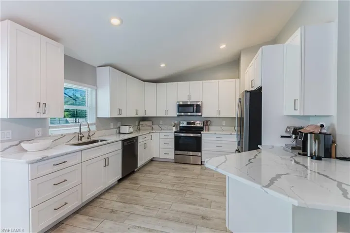 Kitchen featuring white Shaker-style cabinetry, white countertops with grey veining, stainless steel appliances, and wood-finish tile flooring