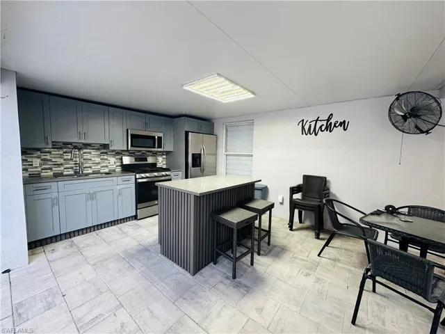 Kitchen with a breakfast bar area, stainless steel appliances, decorative backsplash, a sink, and a kitchen island