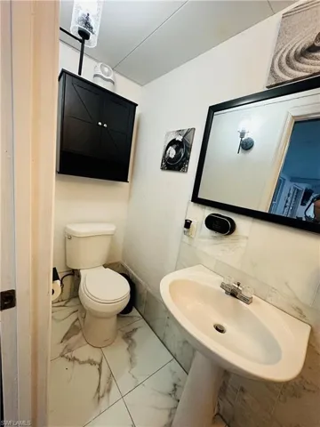 Half bath with marble finish floor, baseboards, a sink, and toilet