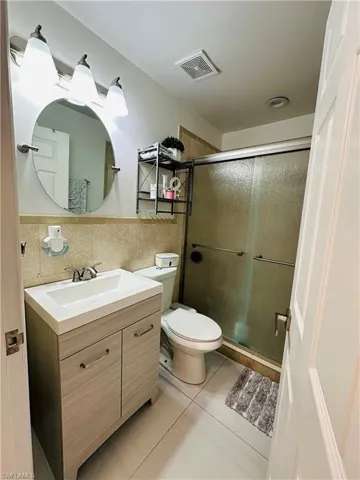 Full bathroom featuring vanity, visible vents, tile walls, a shower stall, and tile patterned floors