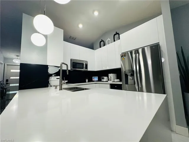 Kitchen featuring pendant lighting, light countertops, appliances with stainless steel finishes, a sink, and modern cabinets