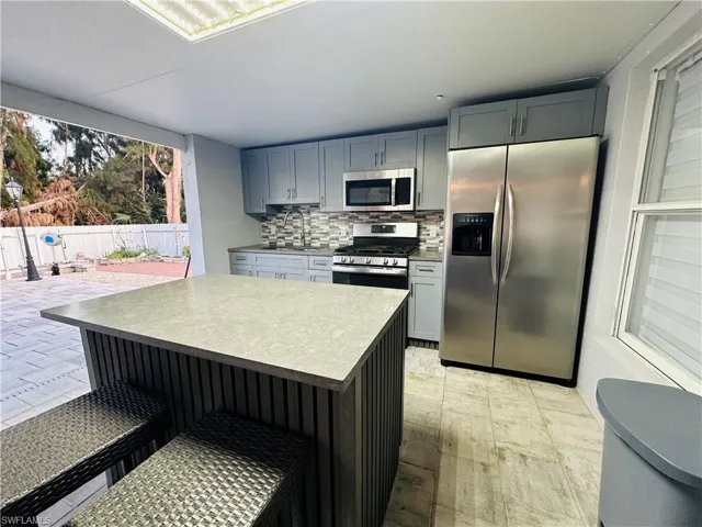 Kitchen with gray cabinetry, stainless steel appliances, a sink, light countertops, and decorative backsplash
