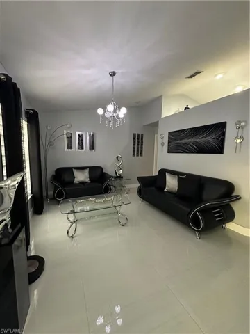 Tiled living area featuring baseboards, visible vents, vaulted ceiling, and a notable chandelier
