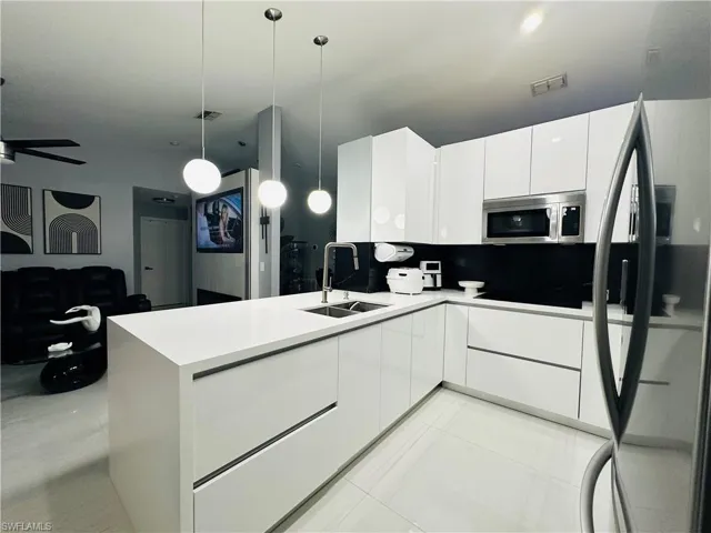 Kitchen featuring modern cabinets, stainless steel microwave, white cabinetry, pendant lighting, and a sink