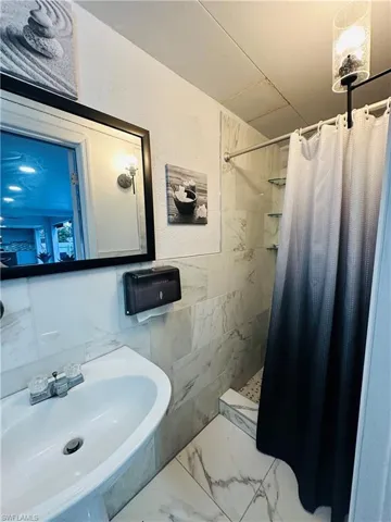 Full bathroom with marble finish floor, a sink, tile walls, and a shower stall