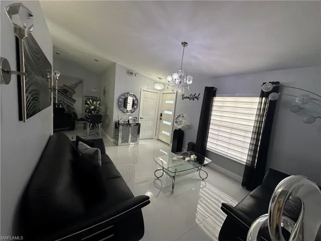 Living room featuring vaulted ceiling, baseboards, visible vents, and a notable chandelier