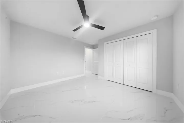 Unfurnished bedroom featuring light marble finish flooring, a ceiling fan, and a closet
