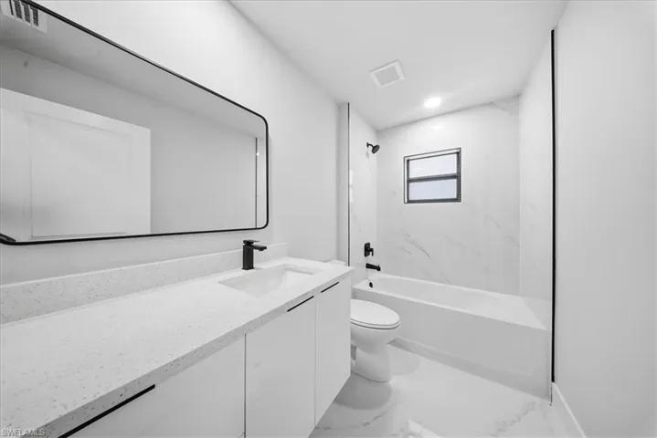 Bathroom with vanity, a combined bath / shower with marble appearance, and light marble finish flooring