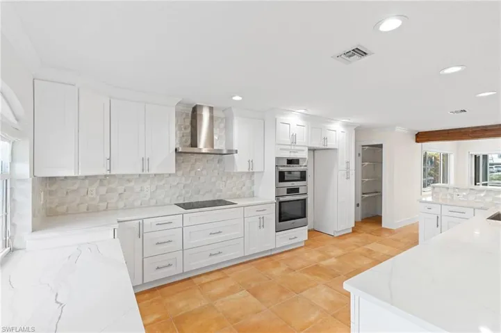 Kitchen featuring backsplash, light stone counters, wall chimney exhaust hood, black electric cooktop, and white cabinets