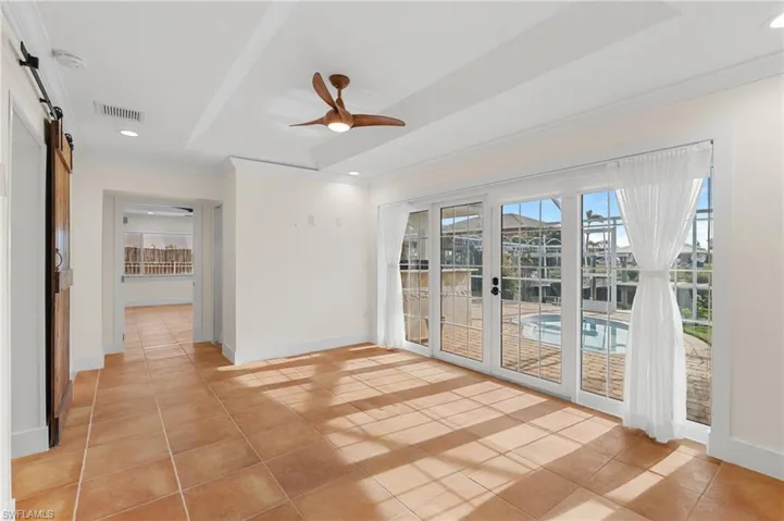 Tiled empty room featuring a barn door, a tray ceiling, ceiling fan, and crown molding