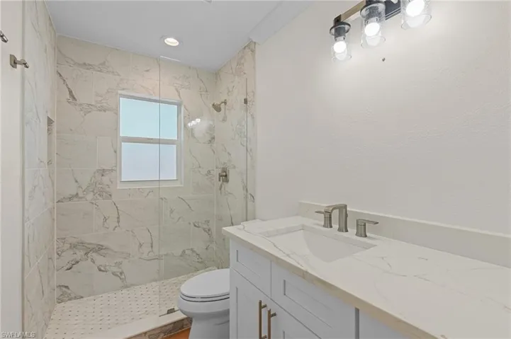 Bathroom featuring tiled shower, vanity, and toilet