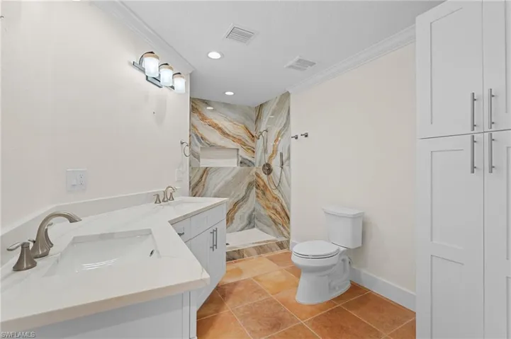 Bathroom with vanity, tile patterned floors, toilet, ornamental molding, and tiled shower