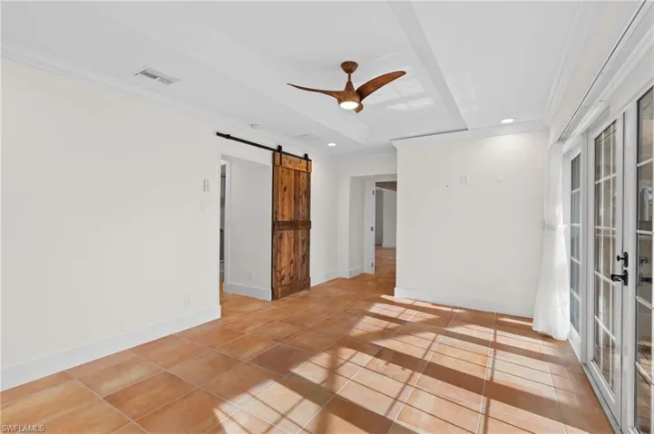 Unfurnished room with tile patterned flooring, ceiling fan, a barn door, ornamental molding, and a tray ceiling