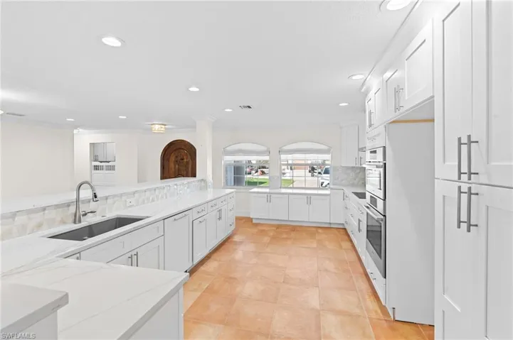 Kitchen with white cabinetry, sink, oven, and light stone counters