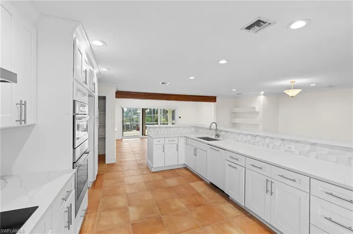 Kitchen with decorative backsplash, kitchen peninsula, black electric cooktop, sink, and white cabinetry