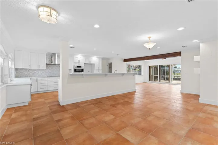 Kitchen featuring tasteful backsplash, stainless steel oven, wall chimney range hood, white cabinets, and a breakfast bar area