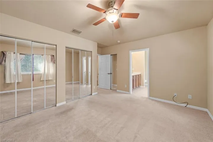 Unfurnished bedroom featuring connected bathroom, two closets, ceiling fan, and light colored carpet