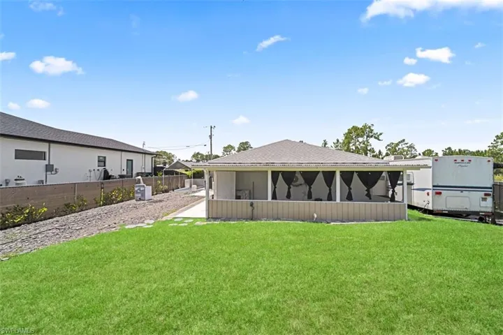 Expansive green lawn with a screened patio, featuring a slatted privacy wall, and a paved walkway leading to an additional structure