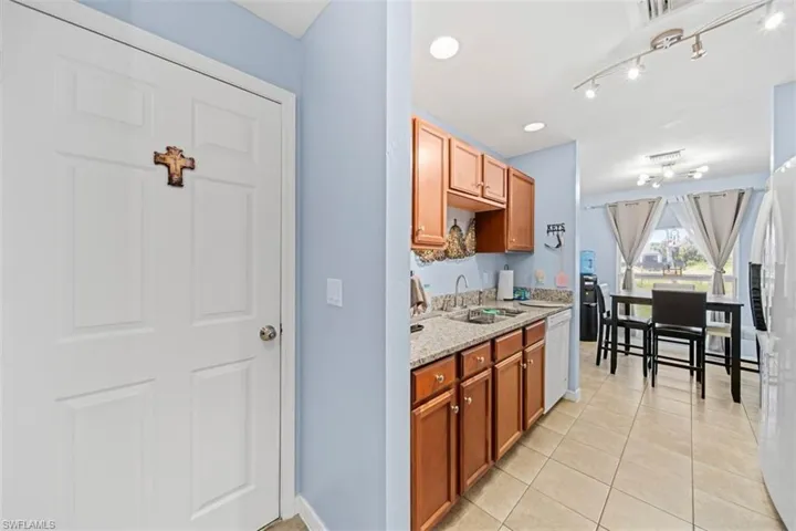 Kitchen area featuring wood cabinetry, granite-style countertops, stainless steel sink, and light tile flooring