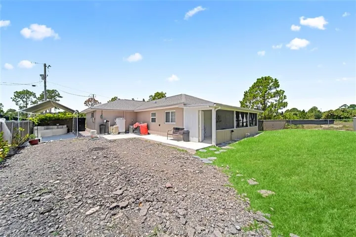 Rear exterior featuring a screened-in porch, a partial concrete patio, and a section of manicured lawn with stepping stones