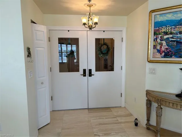 Foyer entrance with french doors, light tile patterned floors, and an inviting chandelier